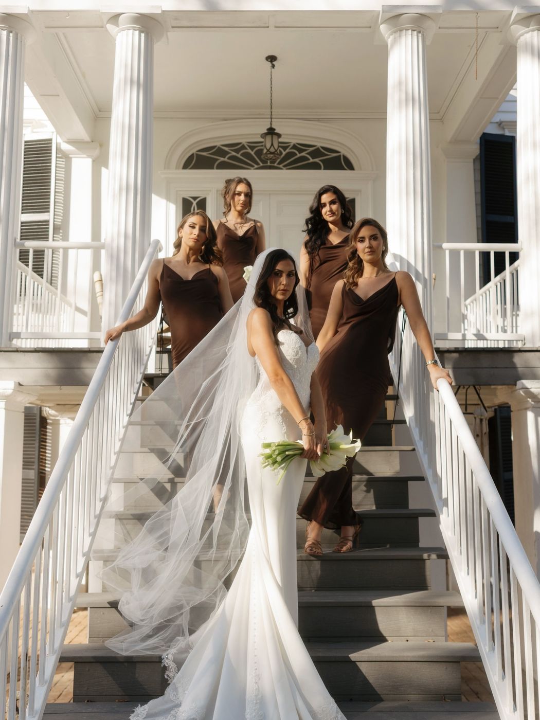 Bride and bridesmaids in chocolate-brown dresses on a grand white staircase