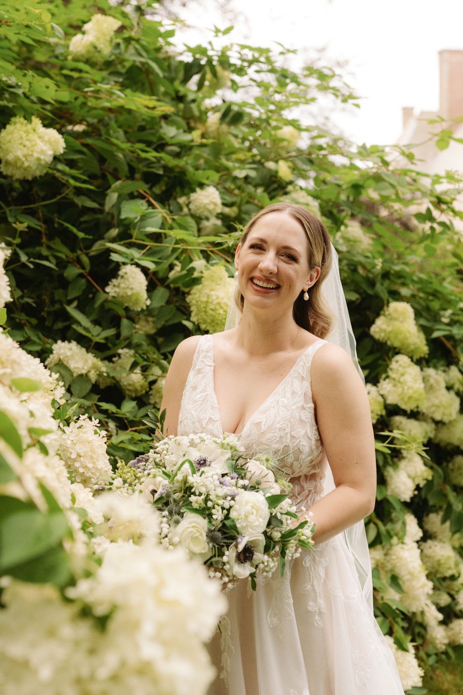 Smiling bride with loose, romantic hair and natural makeup among white hydrangeas