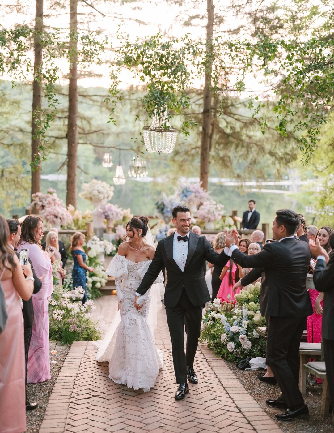 Bride and groom walking up a flower-lined garden aisle after the ceremony